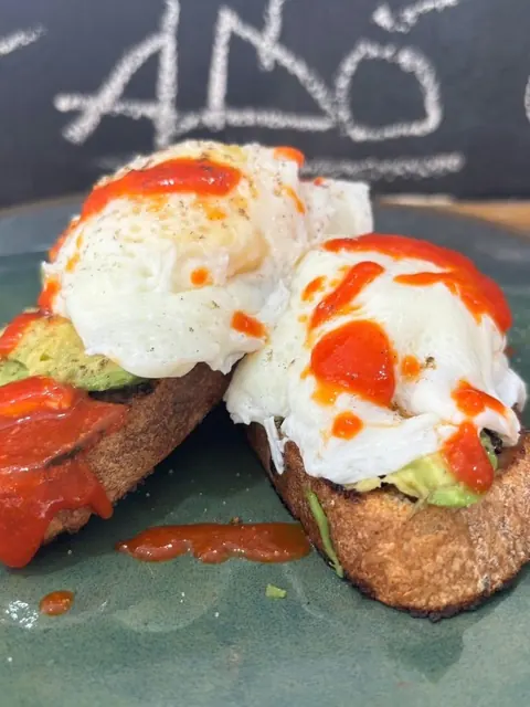Smashed avocado toast topped with poached eggs and chilli sauce.