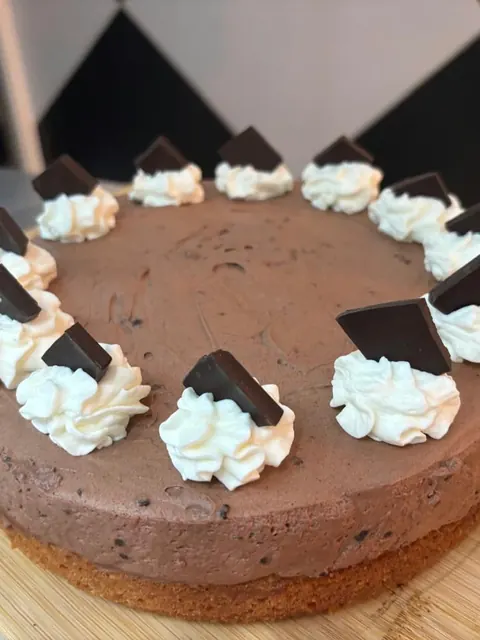 Chocolate cake of the day topped with cream and chocolate squares.