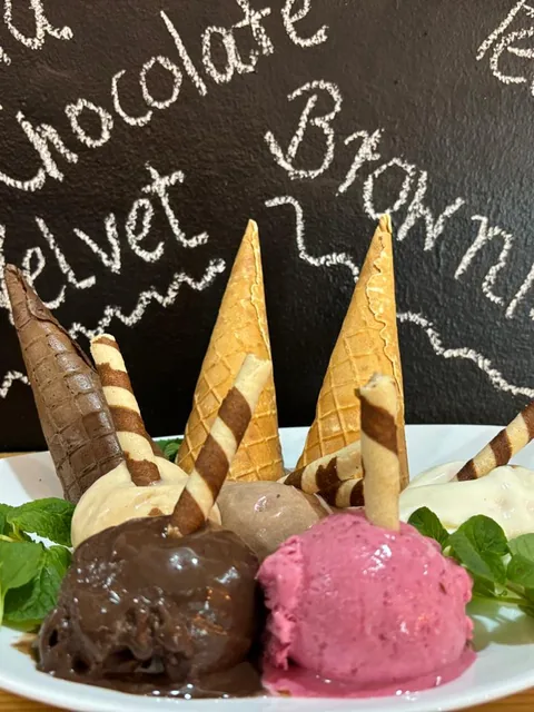Platter of house ice cream scoops with waffle cones, wafer rolls and fresh mint, in front of the flavour board.