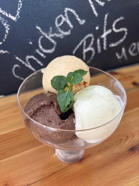 Glass of three house ice cream scoops — chocolate, vanilla and a caramel-toned scoop — with fresh mint.