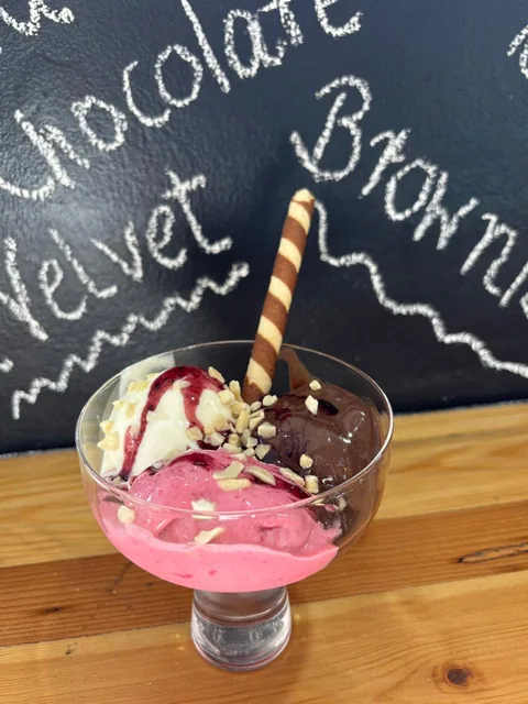 Sundae glass of house ice cream with berry sauce, chopped nuts and a wafer roll.