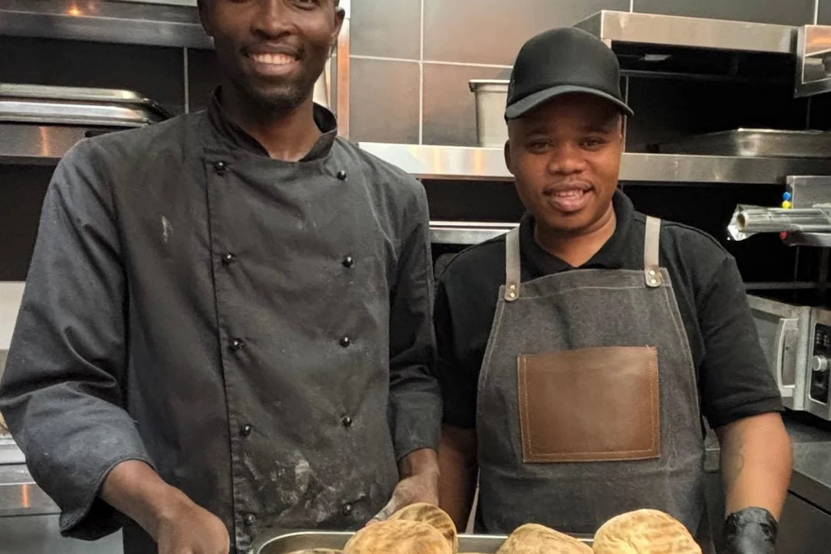 Two smiling Salt & Roost kitchen staff holding a tray of freshly baked rooster brood.