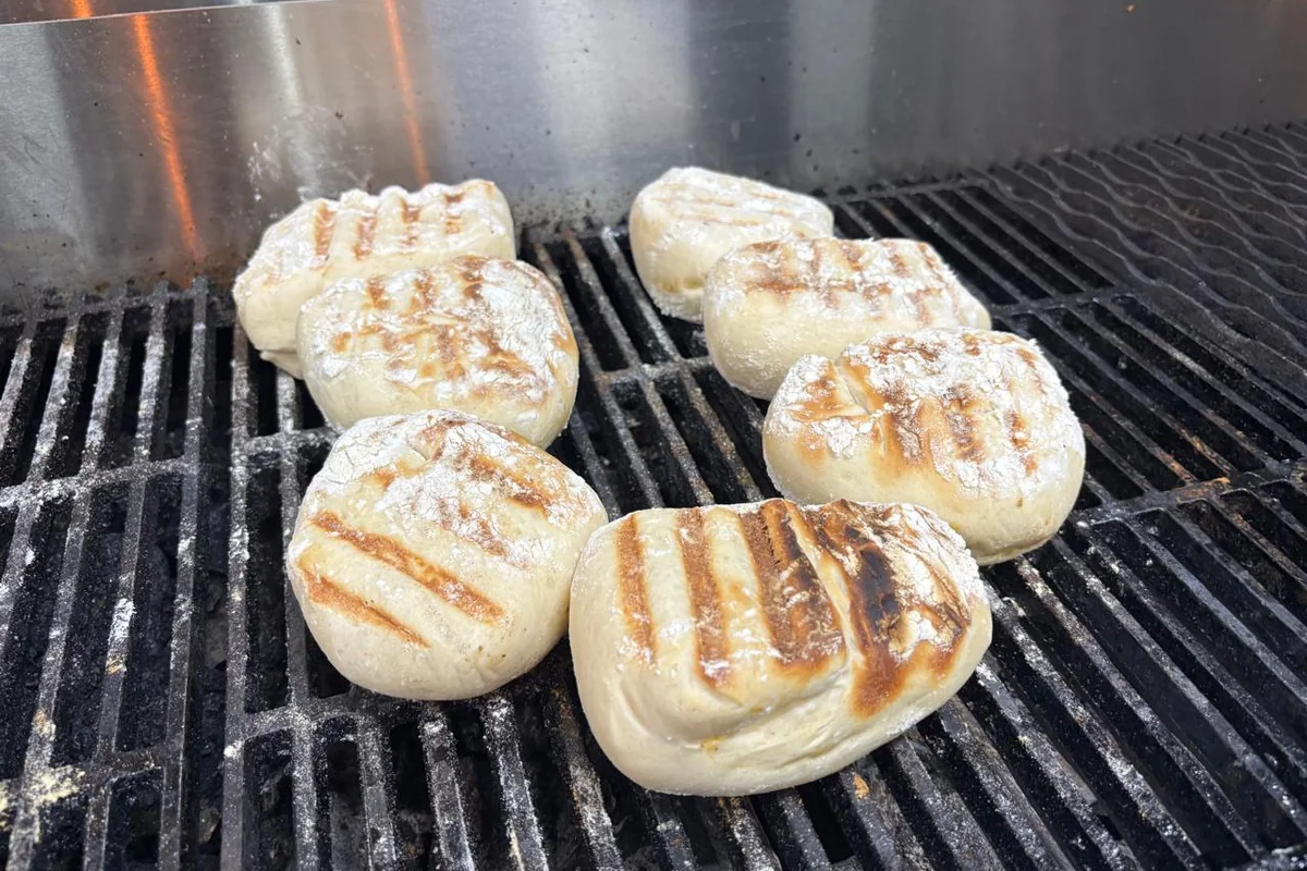 Floured rooster brood rolls toasting over the grill grates at Salt & Roost.