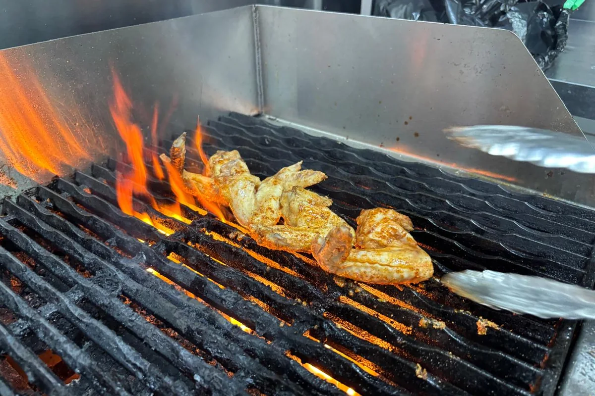 Basted chicken pieces turned with tongs over open flame on the Salt & Roost grill.