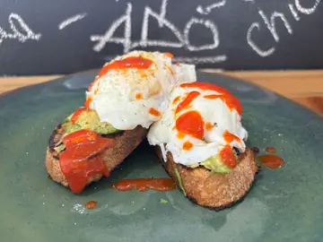 Smashed avocado toast topped with poached eggs and chilli sauce.