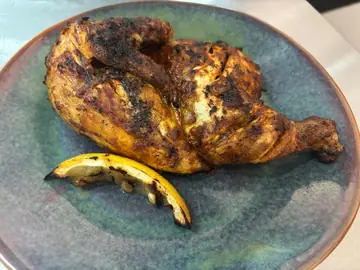 Half flame-grilled chicken with a charred lemon wedge at Salt & Roost.