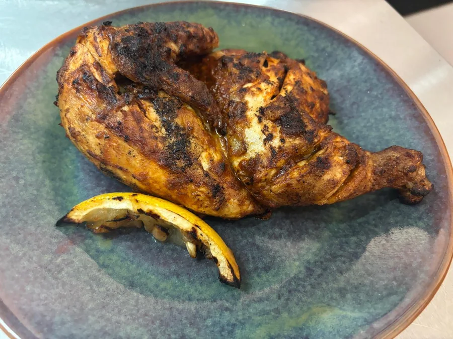 Half flame-grilled chicken with a charred lemon wedge at Salt & Roost.