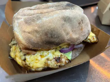 Flame-grilled chicken burger with melted cheese and red onion on rooster brood.