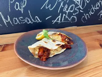 Tikka masala chicken wrap with lemon and coriander in front of the menu chalkboard.